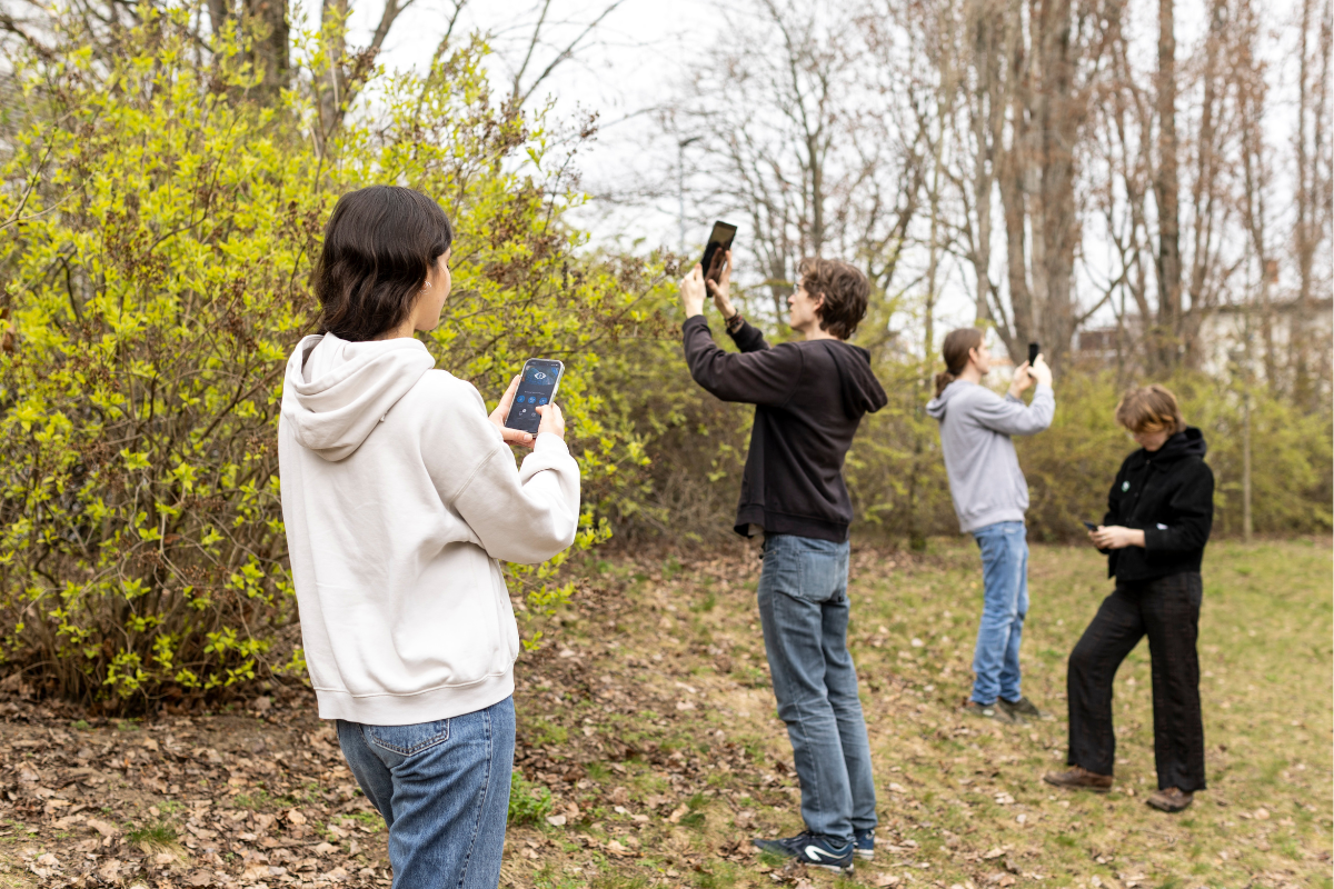Vier Personen mit Handynutzung der Naturblick - App auf einer Wiese stehend. 